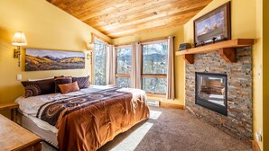 A bedroom with a large bed, a fireplace, and a scenic view through the windows.