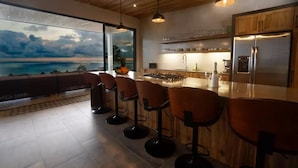 A modern kitchen with a large island, bar stools, and a view of the ocean.