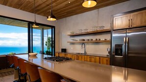 A modern kitchen with a large island, bar stools, stainless steel appliances, and a view of the ocean.