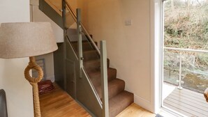 A staircase with a glass railing leading to a landing, a wooden floor, and a lamp with a rope handle. - Riverbank View (Whitby)