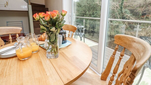 A wooden dining table with a glass vase of flowers, a croissant, and a glass pitcher of orange juice. - Riverbank View (Whitby)