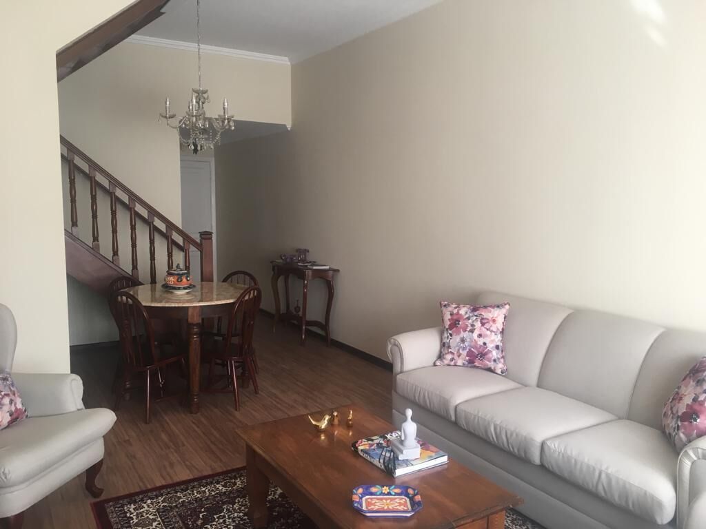 Una sala de estar con sofá, mesa de centro, mesa de comedor, sillas y una araña.