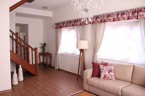 A living room with a wooden staircase, a sofa with floral cushions, a floor lamp, and a chandelier. - Center Suíço Flats e Shopping (Campos do Jordão)