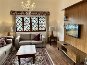 A living room with a sofa, two lamps, a coffee table, a TV, and a patterned rug. - Center Suíço Flats e Shopping (Campos do Jordão)