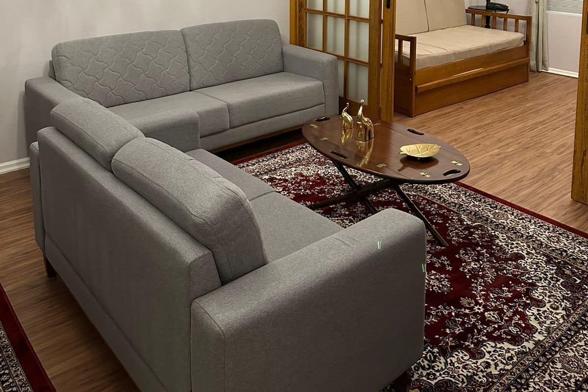 A living room with a grey sectional sofa, a wooden floor, a chandelier, a wooden sliding door, a small table with decorative items, and a framed picture on the wall.