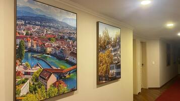 A hallway with two large landscape paintings on the wall, a red carpet, and a wooden floor.