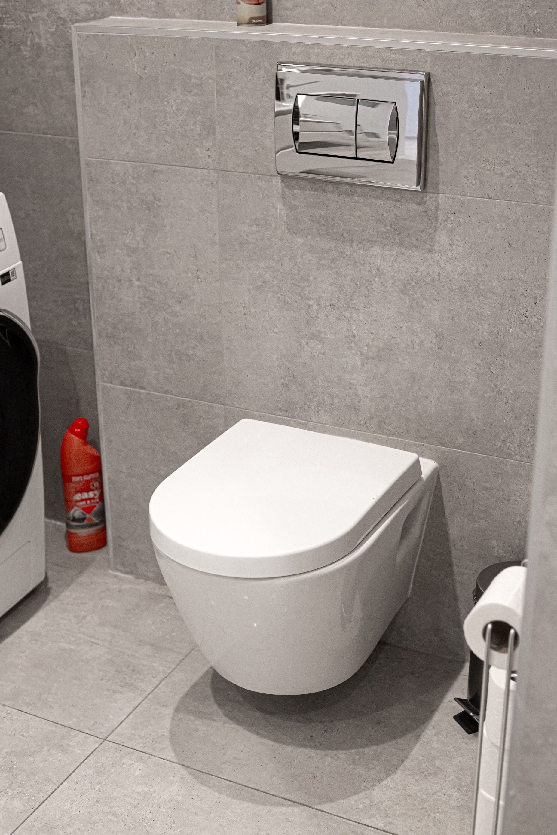 Ein modernes Badezimmer mit Toilette, Handtrockner und einem roten Reinigungszerstäuber.