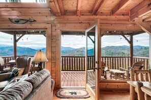 A wooden cabin with a balcony, furnished with a sofa, chairs, and a table. - National Park Mountain Views-Gorgeous Cabin-Cozy Porches-Hot Tub (Sevierville)