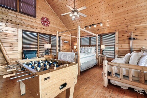 A wooden-floored room with a foosball table, a four-poster bed, and a large window with blinds. - National Park Mountain Views-Gorgeous Cabin-Cozy Porches-Hot Tub (Sevierville)