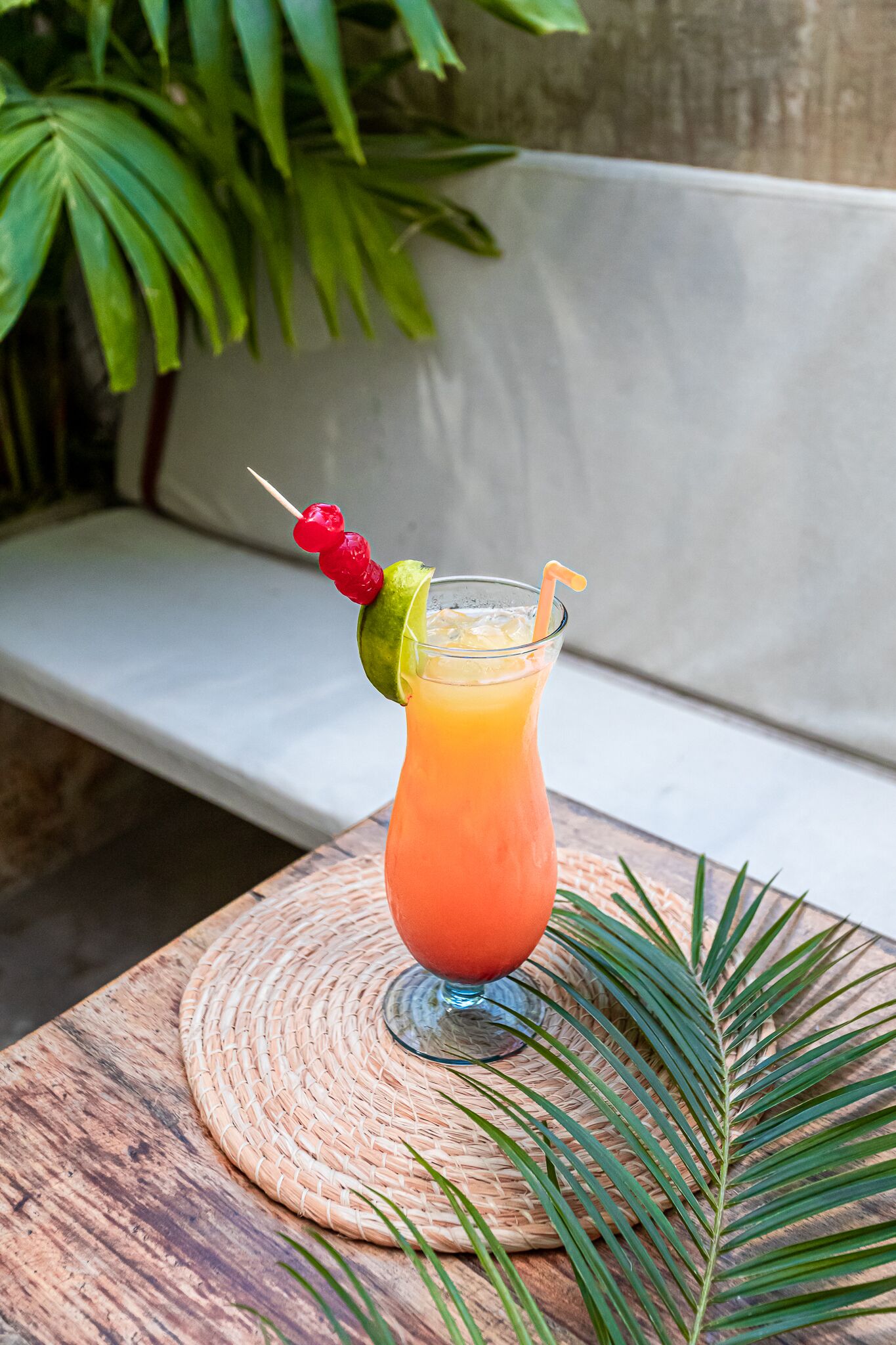 A glass of orange juice with a fruit skewer on a woven placemat.