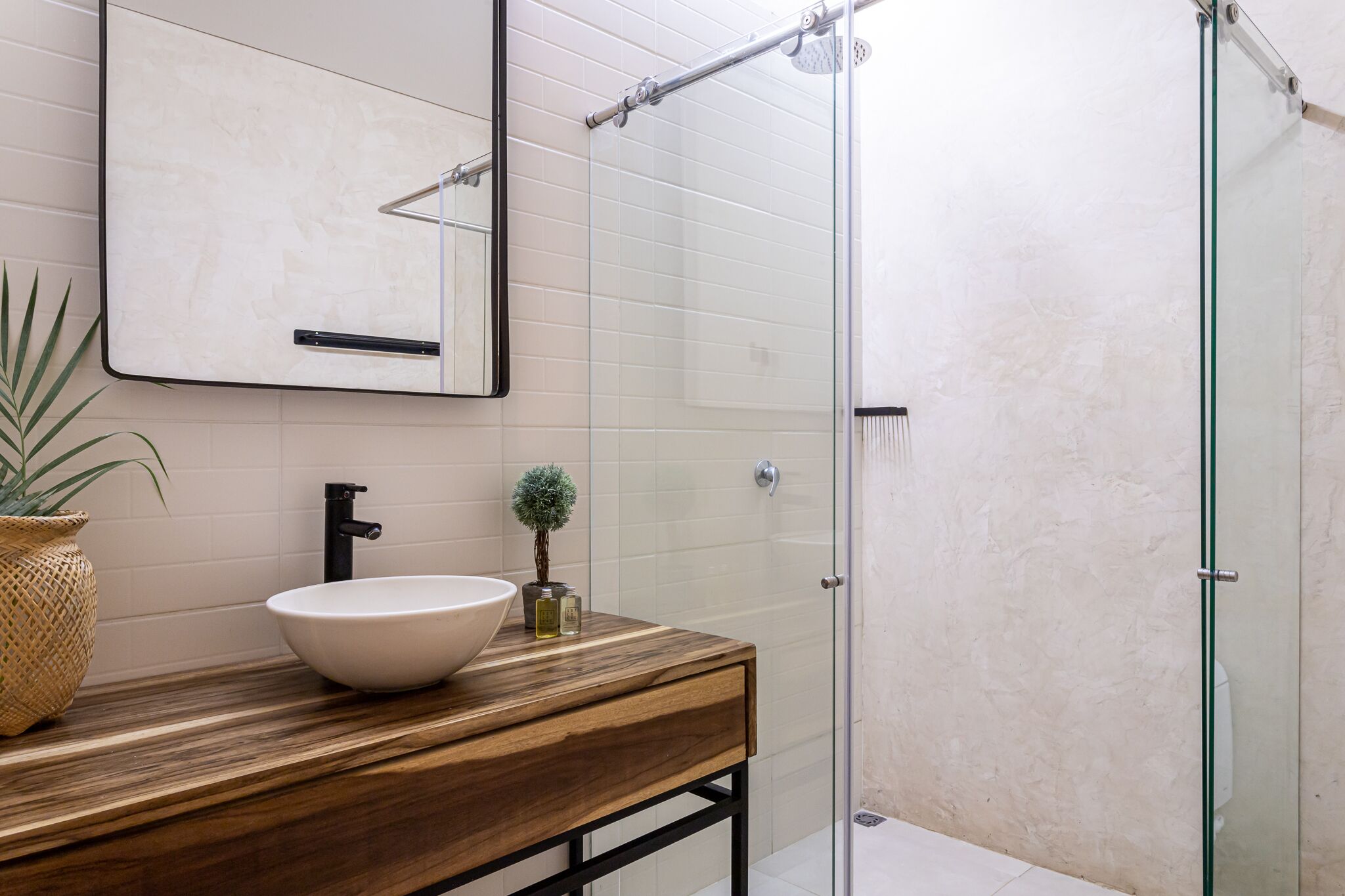 Un baño con tocador de madera, un lavabo blanco, un espejo y una mampara de vidrio para la ducha.
