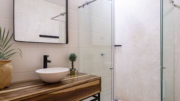 Une salle de bain avec un meuble-lavabo en bois, un lavabo blanc, un miroir et une cabine de douche en verre.