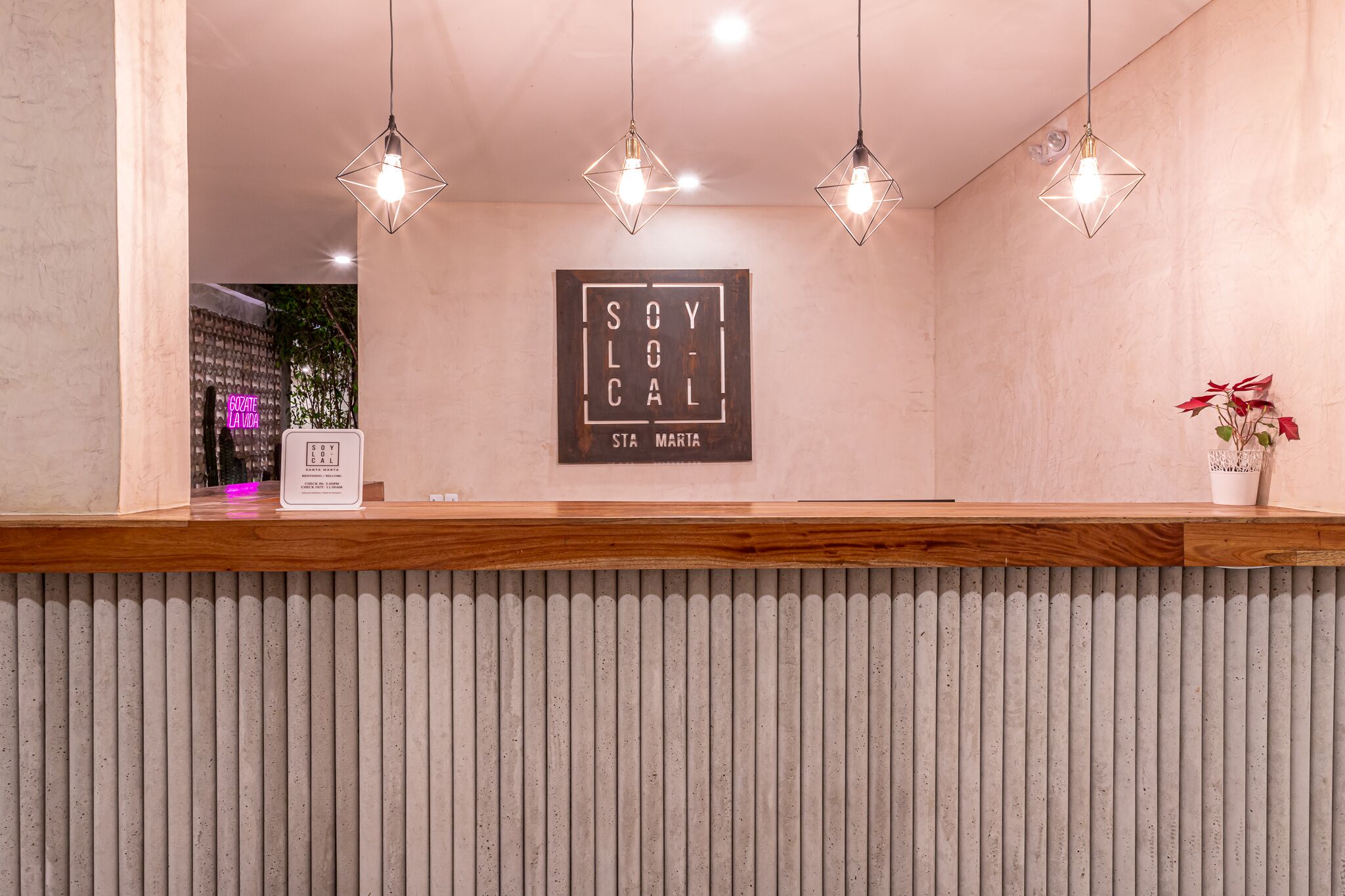Un área de recepción con mostrador de madera, un letrero de neón y un texto enmarcado en la pared.