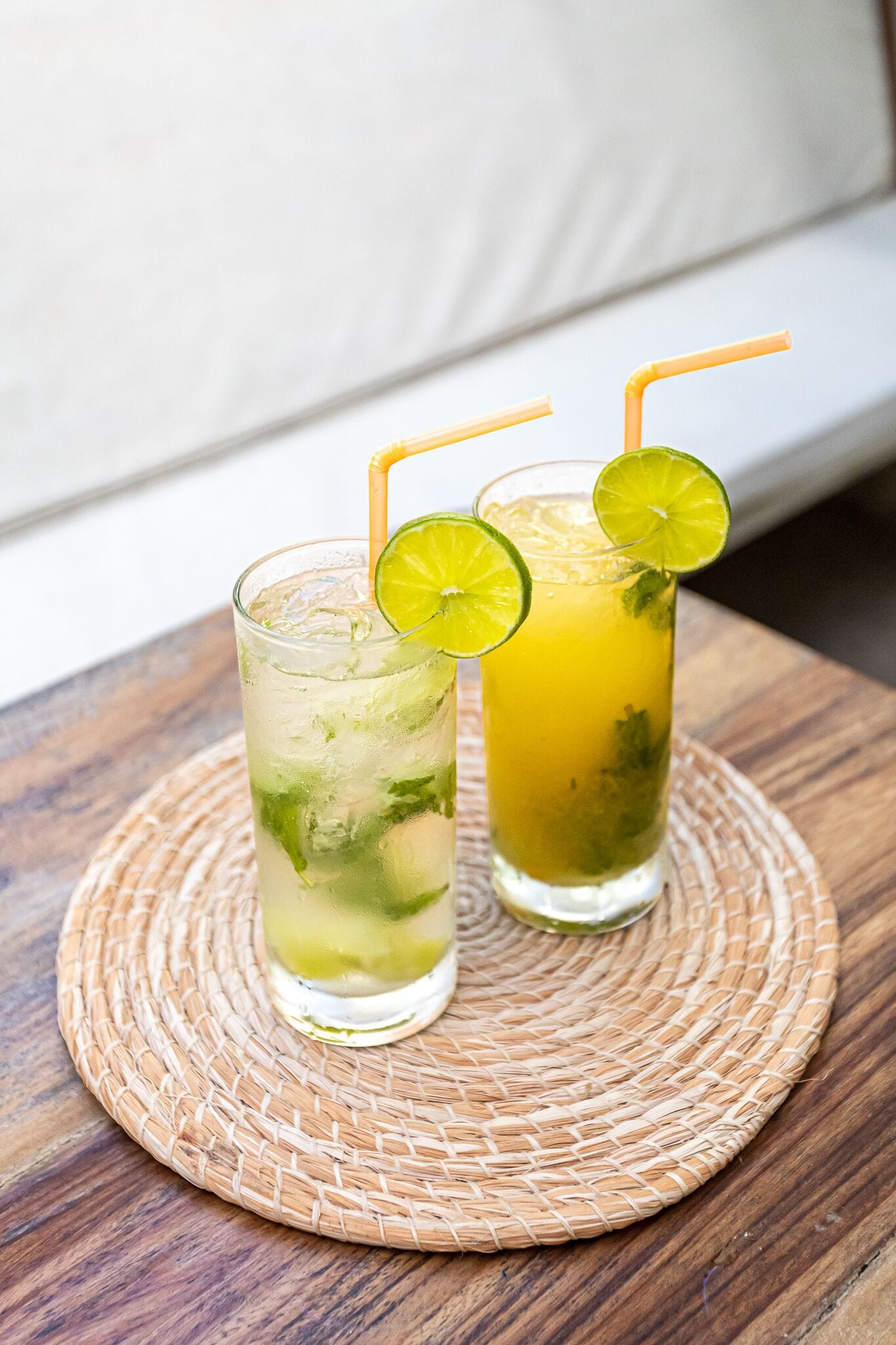 Two glasses of iced drinks with lime garnishes on a woven placemat.