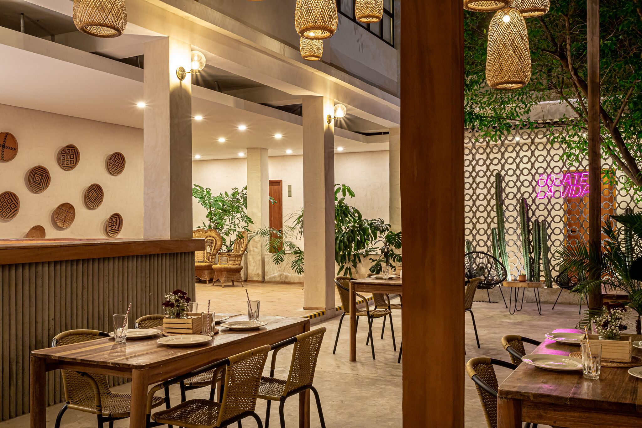 A restaurant with wooden tables and chairs, decorative wall plates, and hanging wicker lamps.