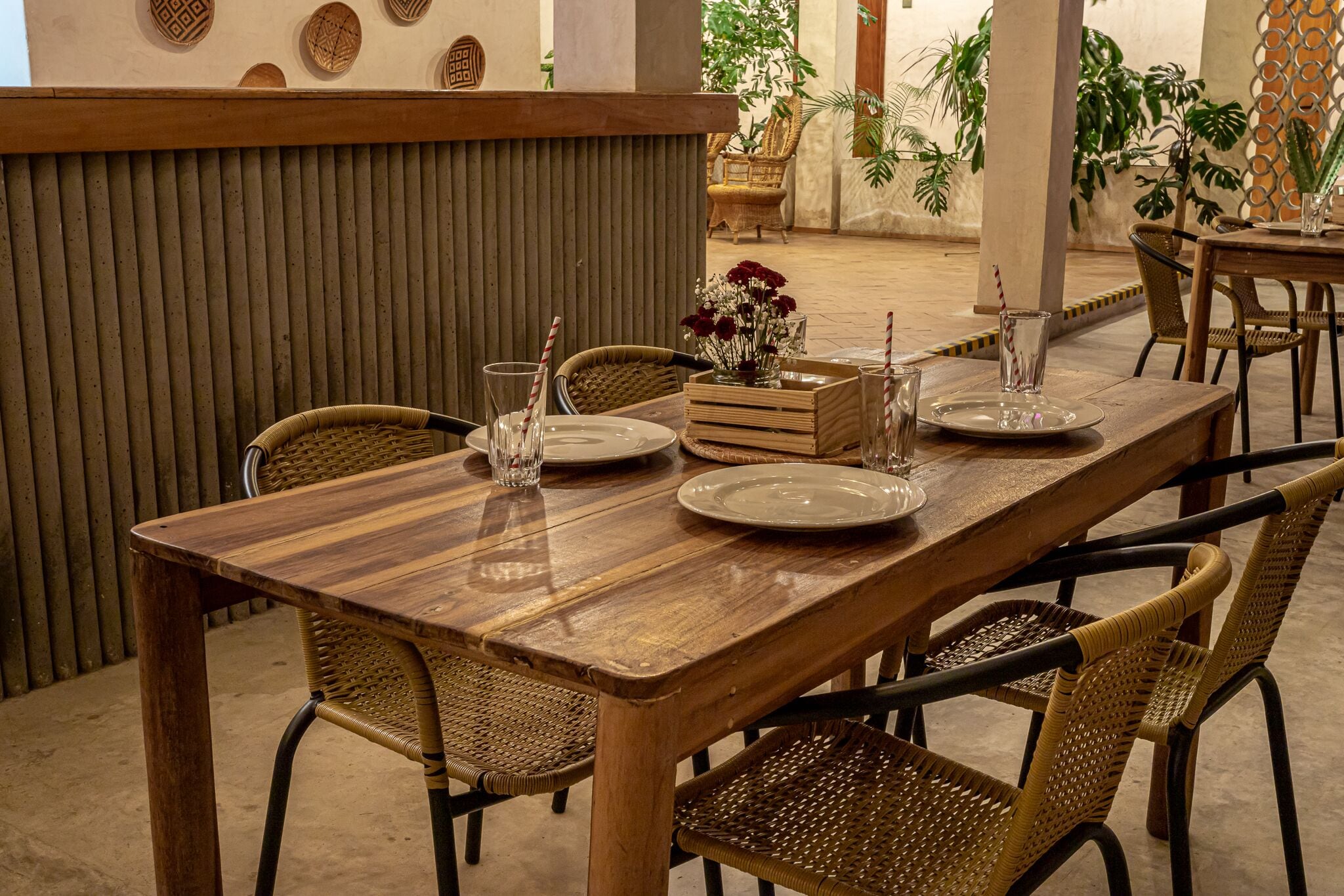 A wooden dining table with wicker chairs, a vase with flowers, and a tray with plates and glasses.