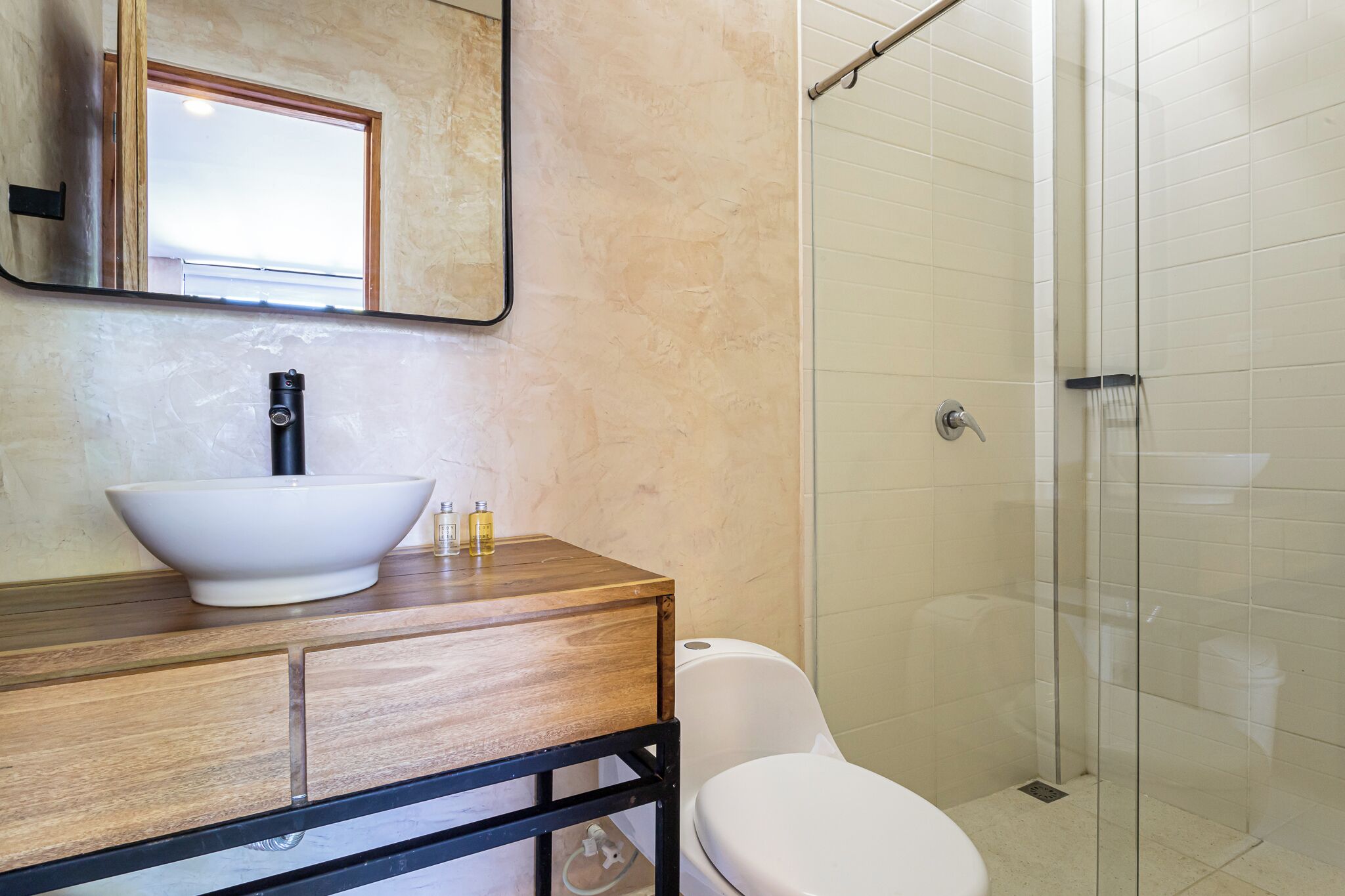 Een badkamer met een houten wastafelmeubel, een witte wasbak, een spiegel, een toilet en een douche met glazen wanden.