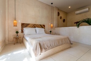 Une chambre à coucher avec un lit, deux tables de chevet, une petite plante en pot et un climatiseur fixé au mur.