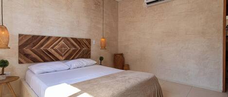 Un dormitorio con cama, lámpara colgante, una mesita con una planta y un equipo de aire acondicionado.