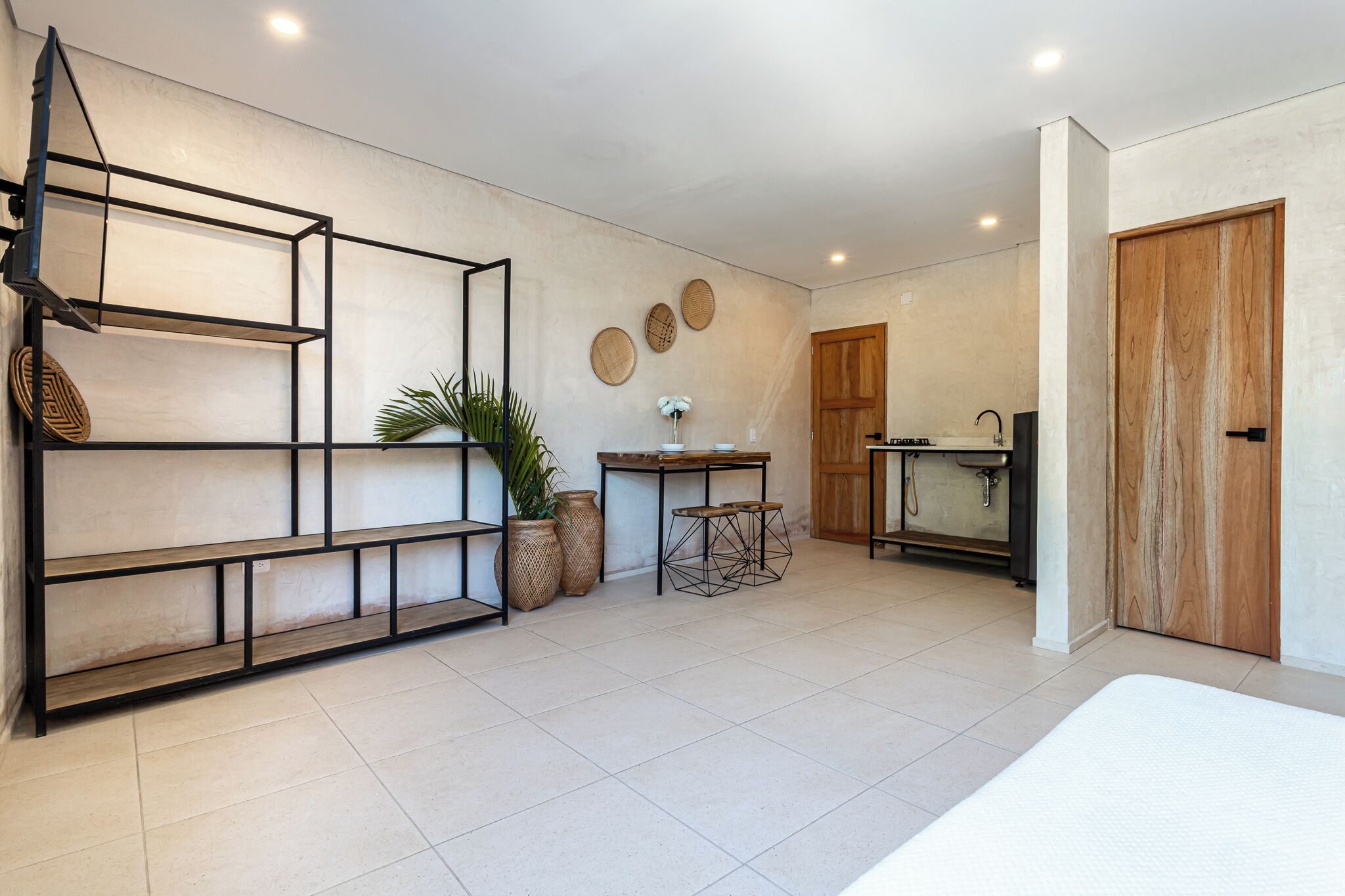 A modern kitchen with a wooden door, a built-in sink, and a small table with stools.