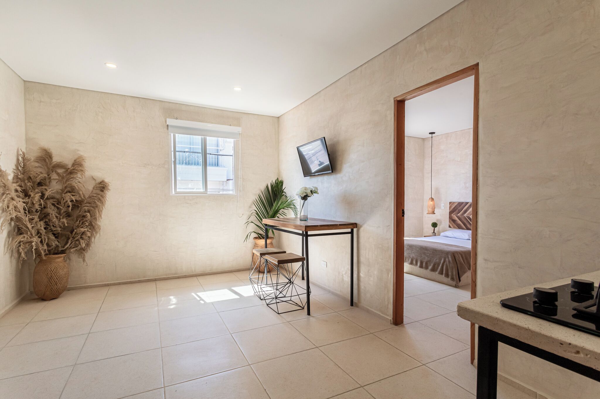 A modern hotel room with a large window, a dining area with a table and chairs, and a bed with a view.