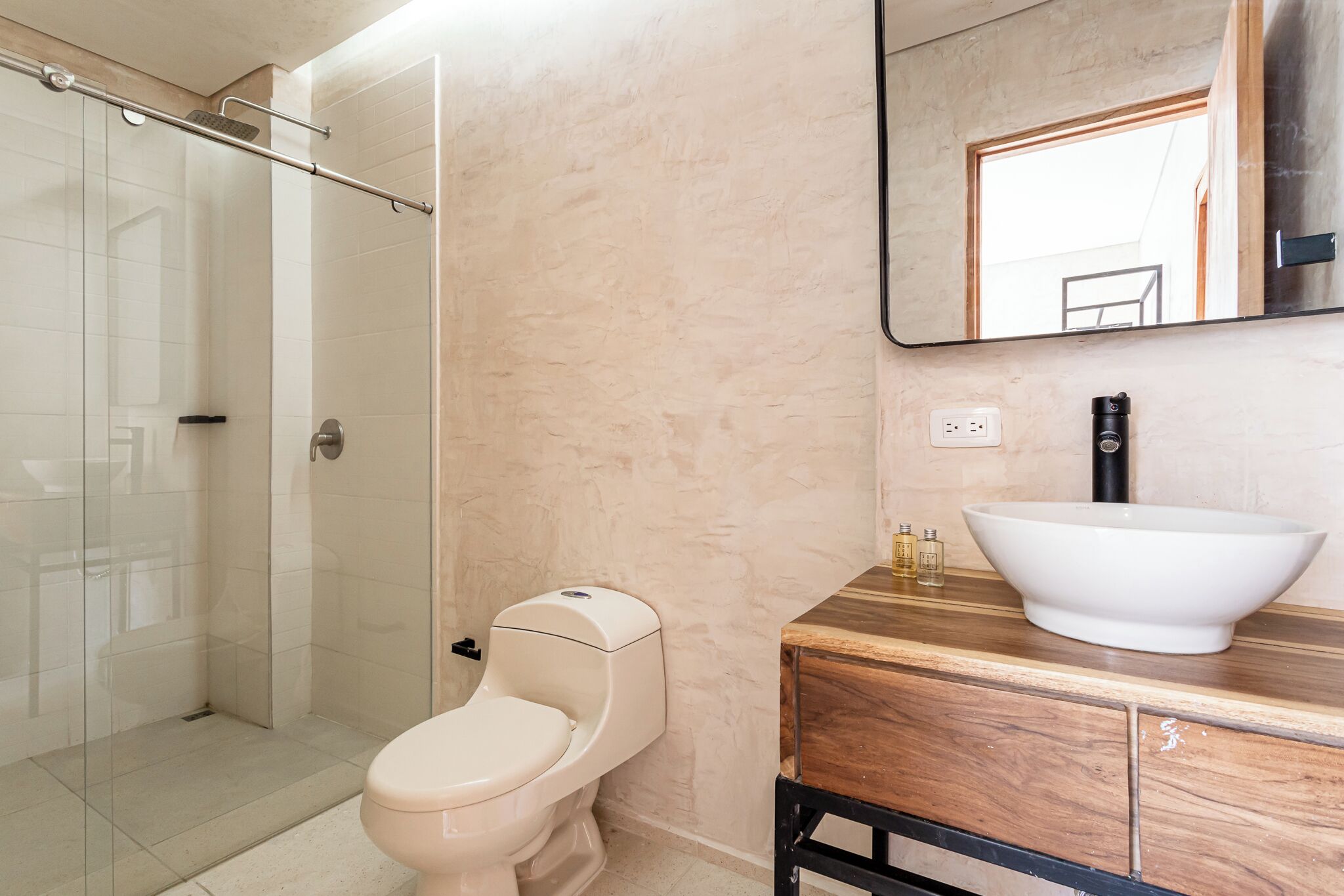 A bathroom with a glass shower enclosure, a toilet, a wooden vanity with a large vessel sink, and a mirror above the sink.