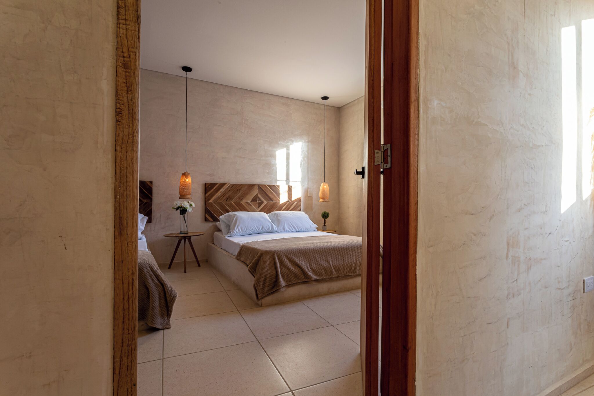 Une chambre à coucher avec un lit, des tables de chevet, un luminaire suspendu et une vue sur l’extérieur.