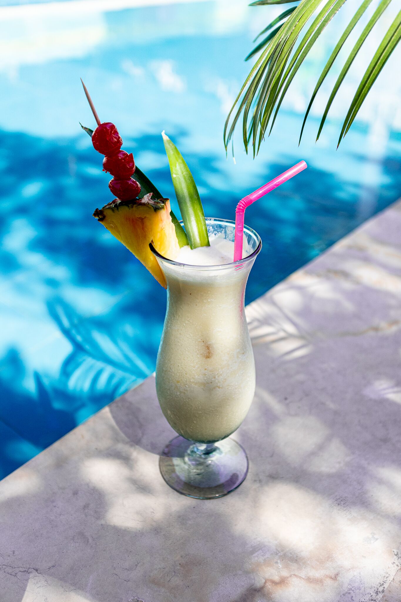 Cóctel con piña y pajita, sobre una mesa junto a una piscina.