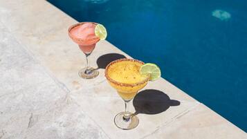 Two margaritas on a poolside table with a pool in the background.
