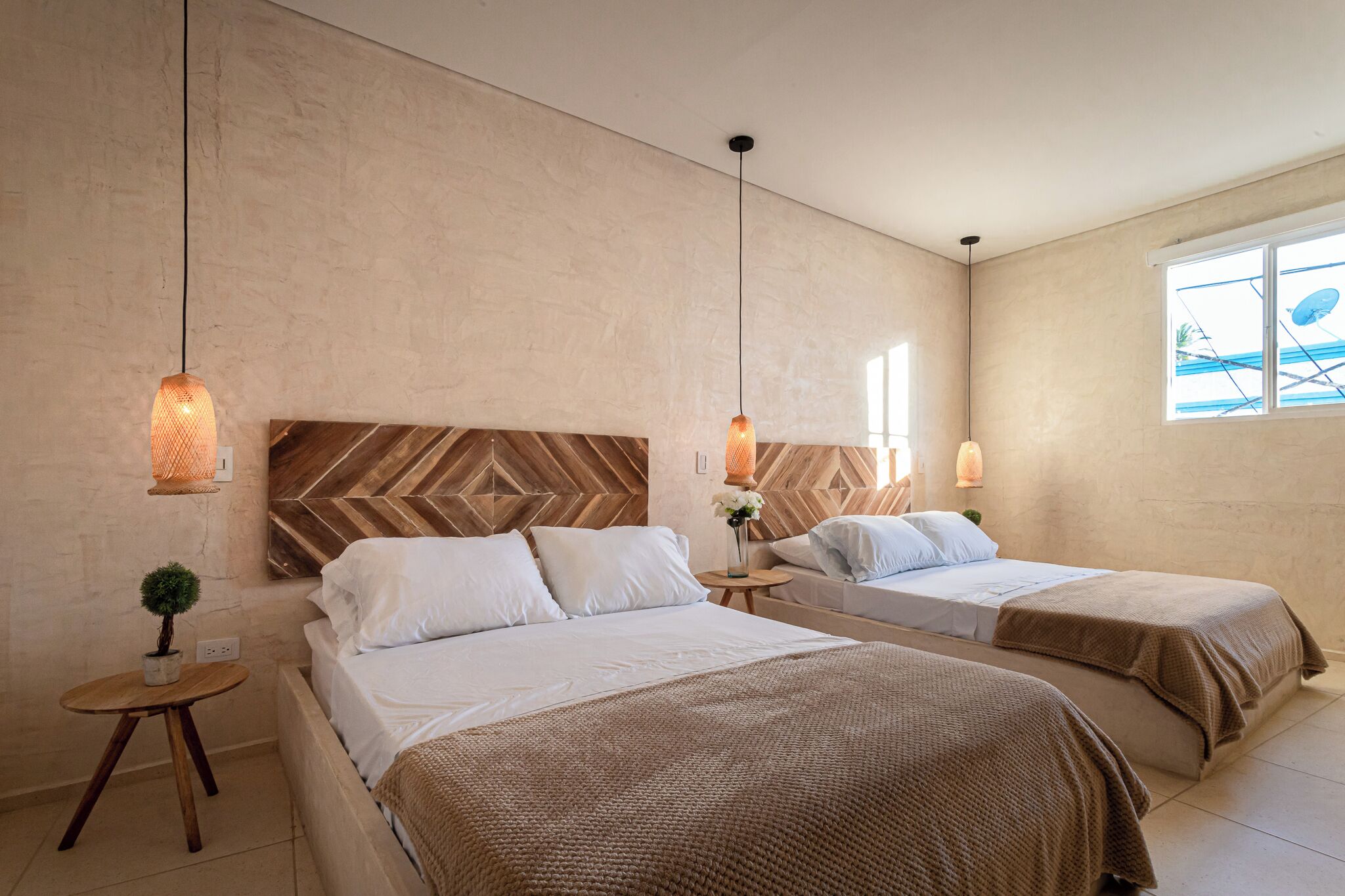 A hotel room with two beds, a large window, and a herringbone-patterned headboard.