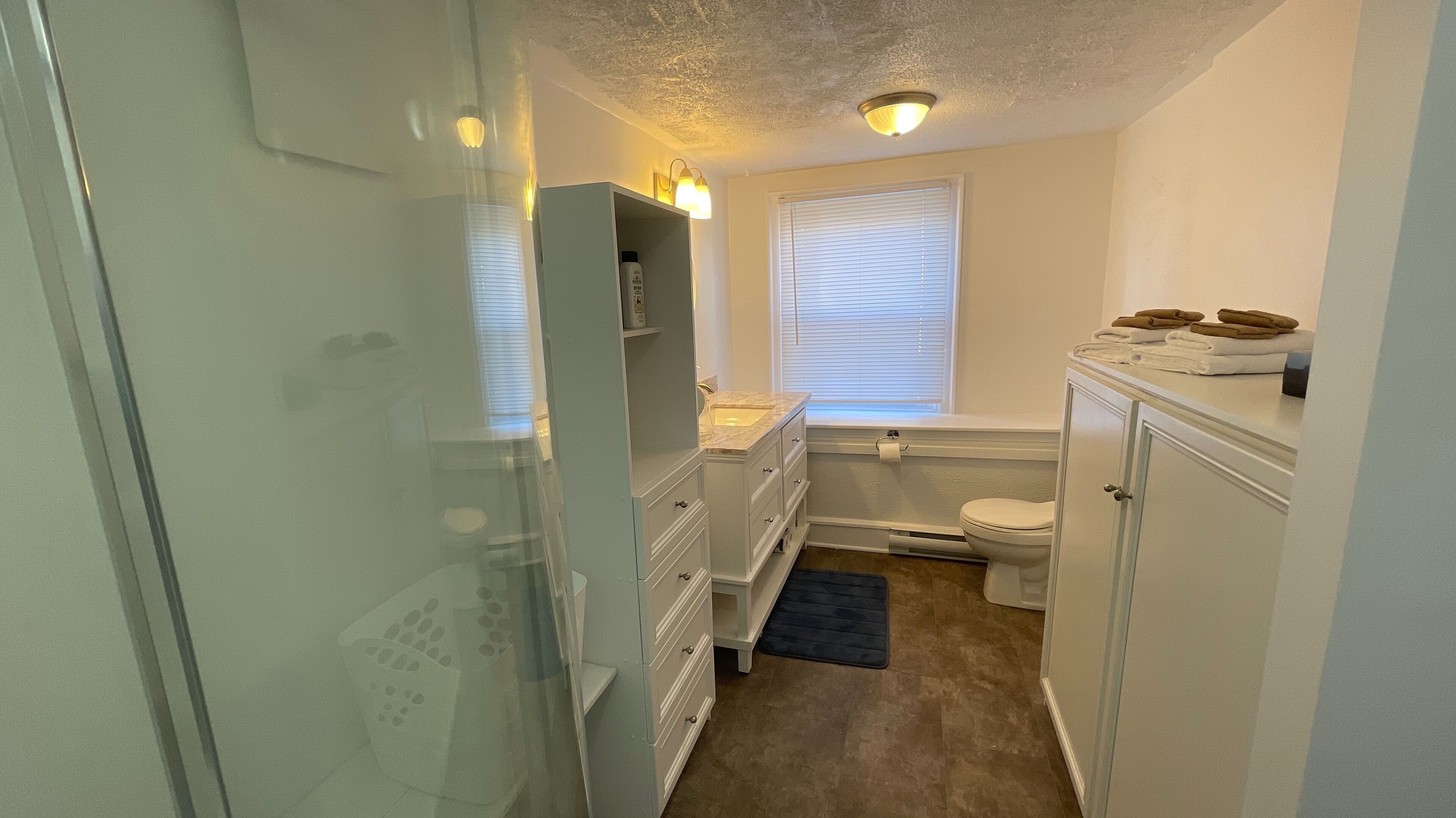 A narrow bathroom with a toilet, sink, and storage cabinets.