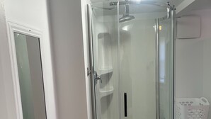 A glass-enclosed shower with a white tiled floor and a blue mat. - Studio-like Comfort in Wolfville’s Beating Heart (Wolfville)