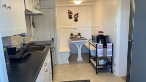 A compact kitchen with white cabinetry, a black countertop, a small island with a sink, and a coffee maker. - Studio-like Comfort in Wolfville’s Beating Heart (Wolfville)