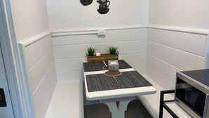 A small, white-walled room with a white table, two potted plants, a candle, and a microwave. - Studio-like Comfort in Wolfville’s Beating Heart (Wolfville)