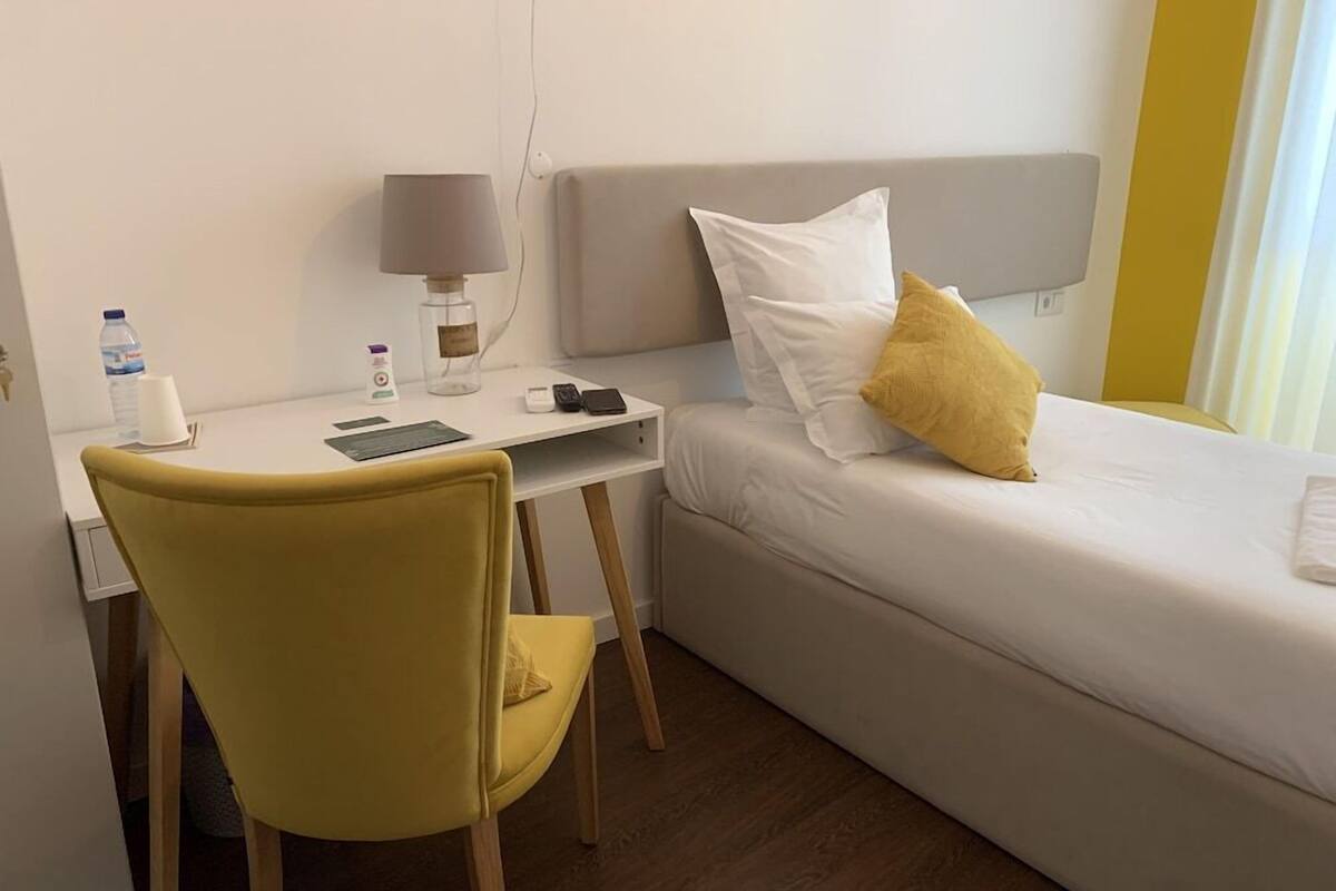 A hotel room with a bed, a desk, a chair, a lamp, and a bedside table.