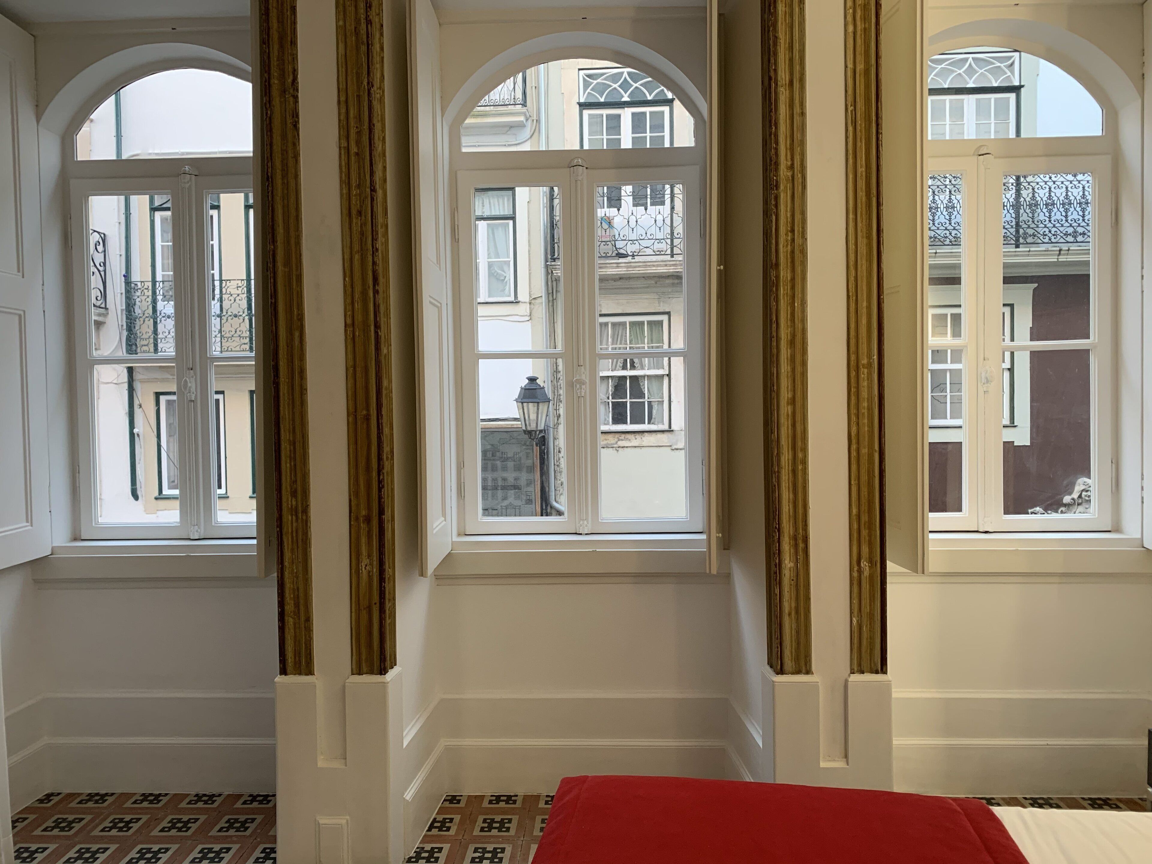A room with three large arched windows, white walls, and a patterned floor.