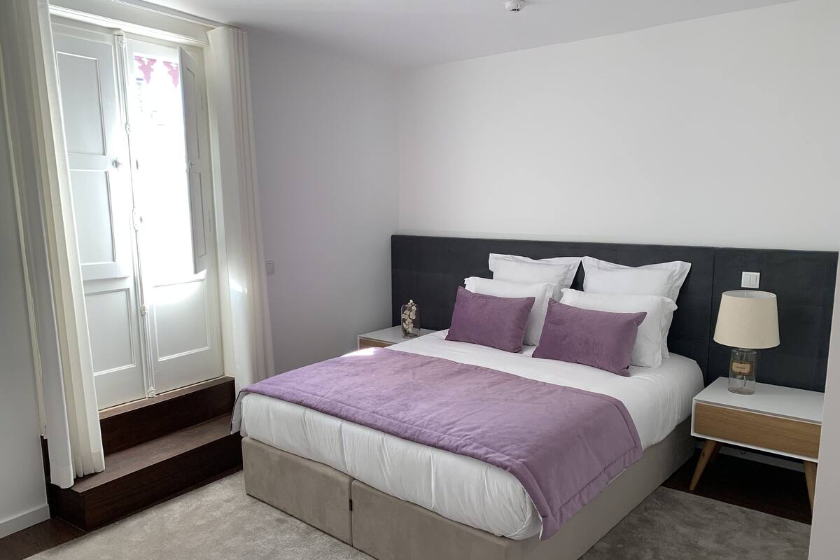 A bedroom with a bed, nightstands, a lamp, and a window with curtains.