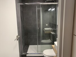Un baño moderno con ducha envuelta en vidrio, inodoro blanco y lavamanos.