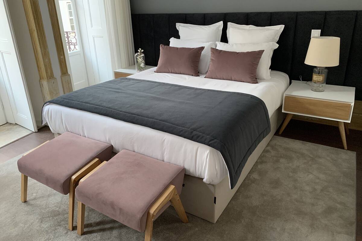 A neatly made bed with a grey and white duvet, two bedside tables with lamps, and a bench at the foot of the bed.