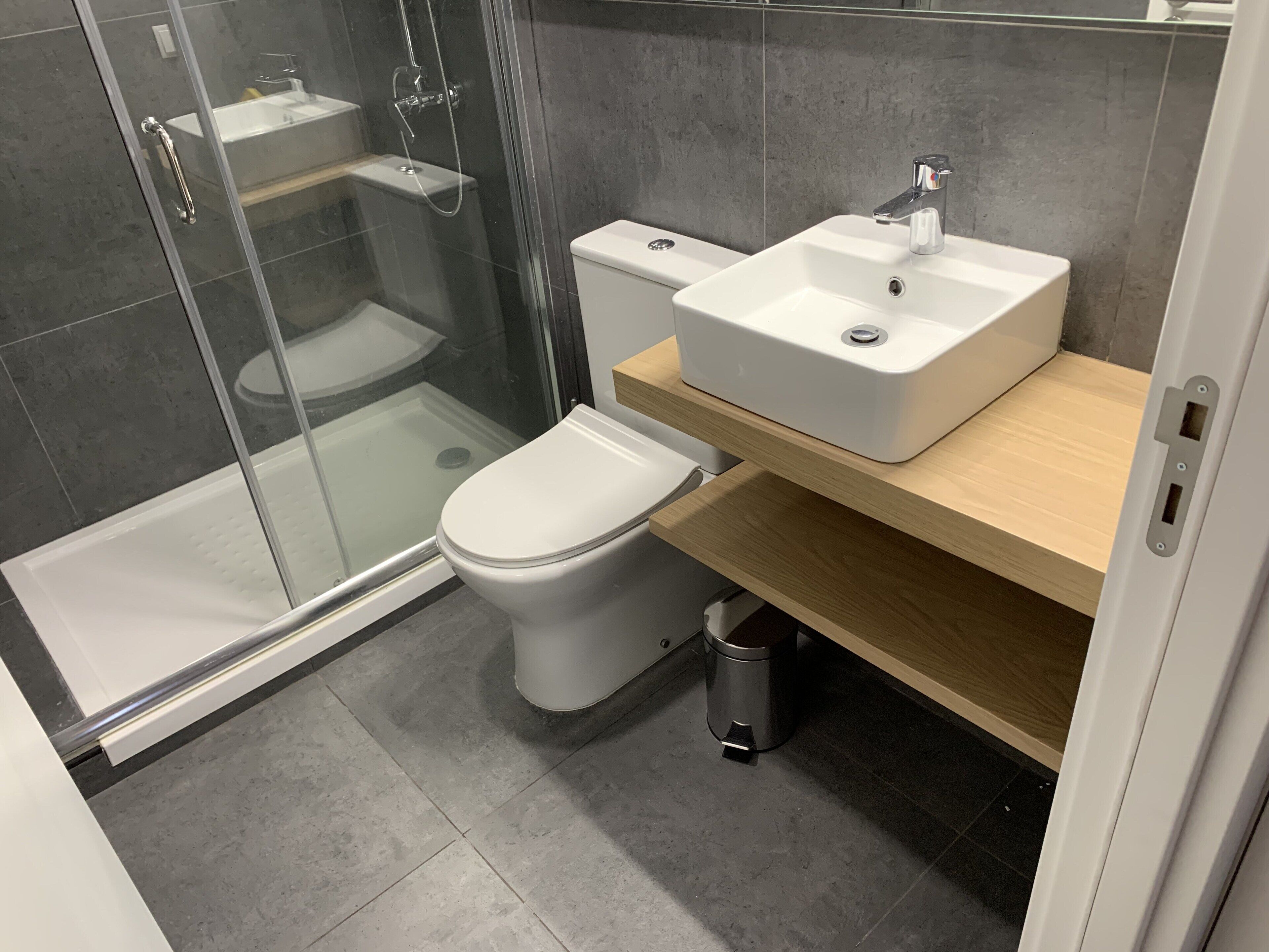 A modern bathroom with a glass-enclosed shower, a white toilet, and a wooden vanity with a sink.