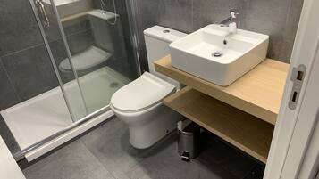 A modern bathroom with a glass-enclosed shower, a white toilet, and a wooden vanity with a sink.