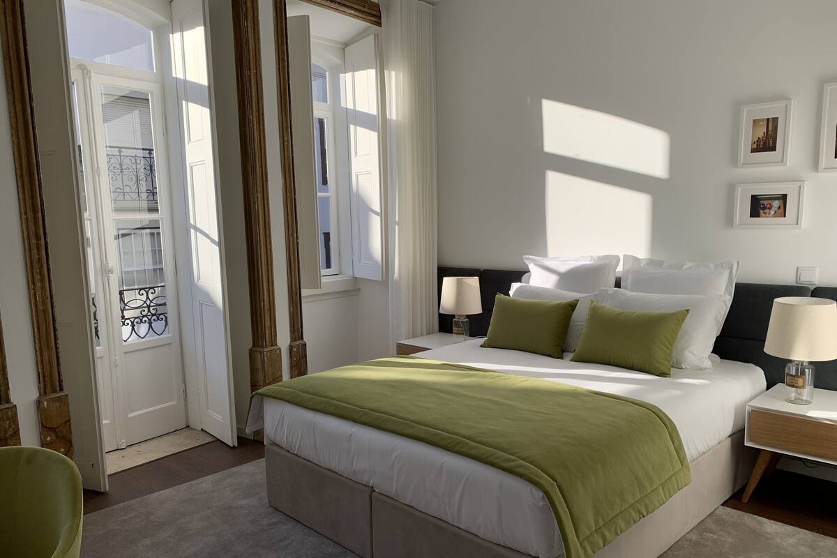 A hotel room with a large bed, two bedside tables with lamps, a view of the outside balcony, and a door with a window.