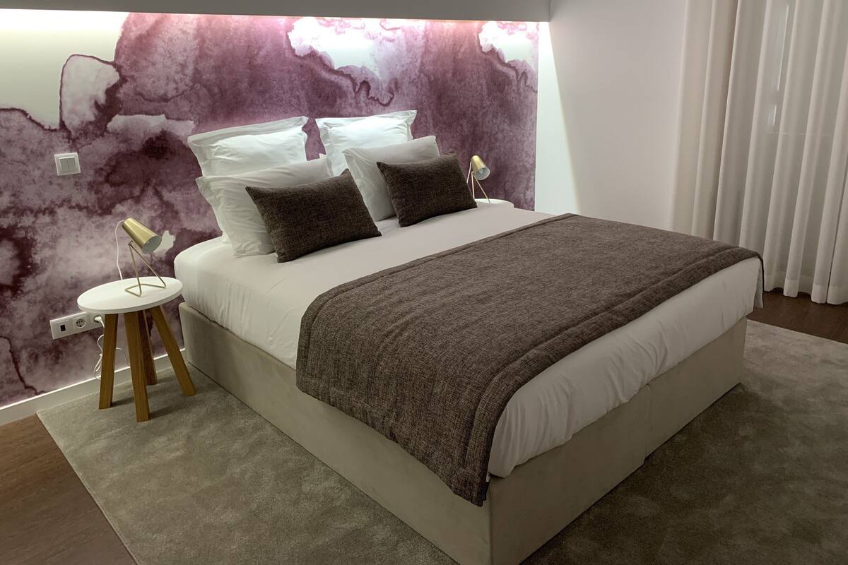A modern bedroom with a large bed, a marble wall, a bedside lamp, and a small table.