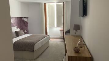Een moderne hotelkamer met een groot bed, een houten bureau, een lamp en een flatscreen televisie die aan de muur is bevestigd.