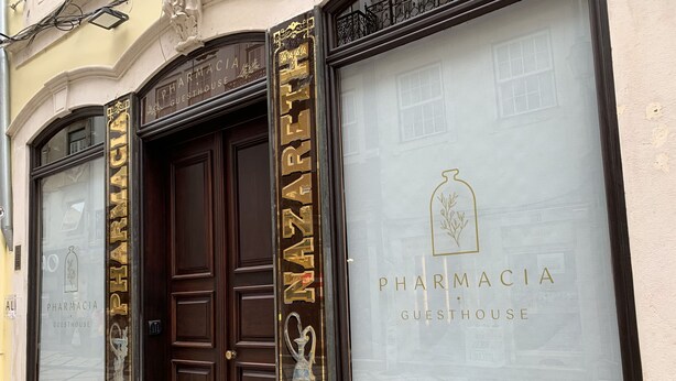 En byggnadsfasad med en skylt som visar texten ”PHARMACIA GUESTHOUSE”.