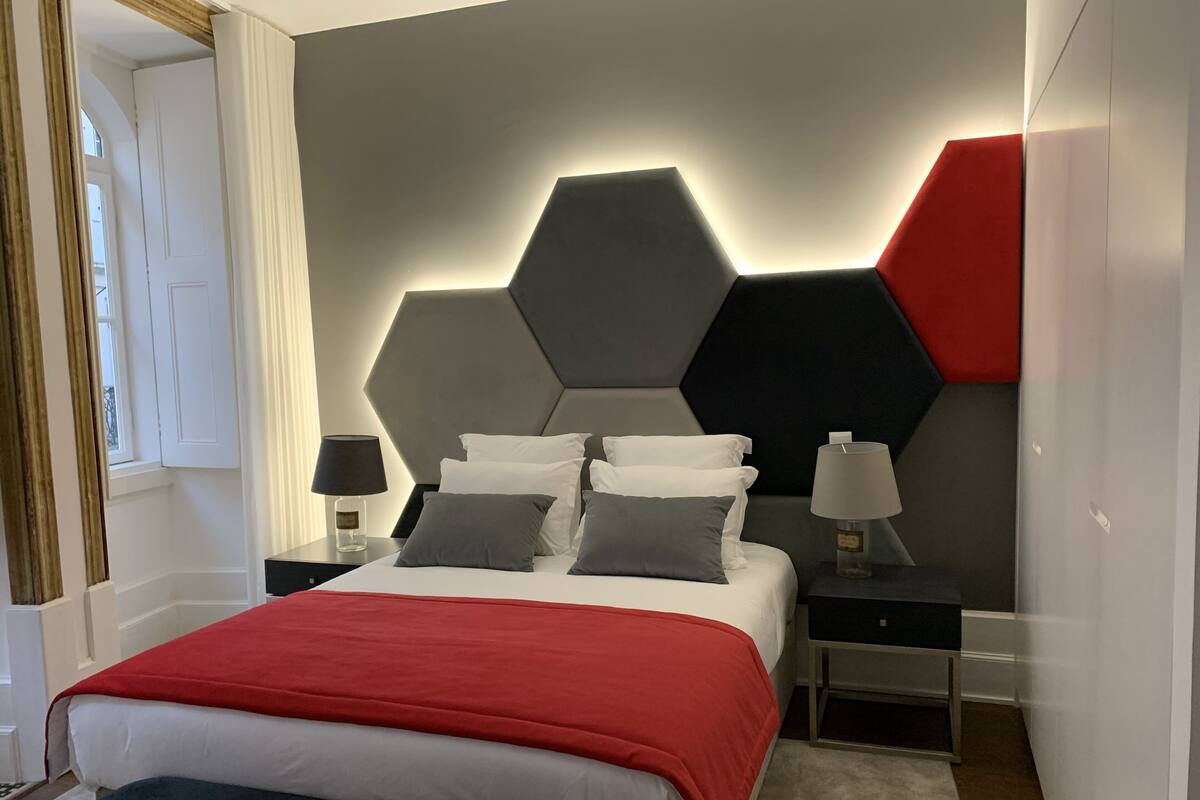 A modern bedroom with a large bed, two bedside tables, and a geometric wall design.