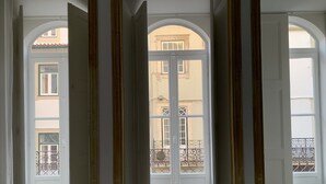 Ett rum med ett stort, välvt fönster, träkolonner och utsikt över en byggnad med balkonger.