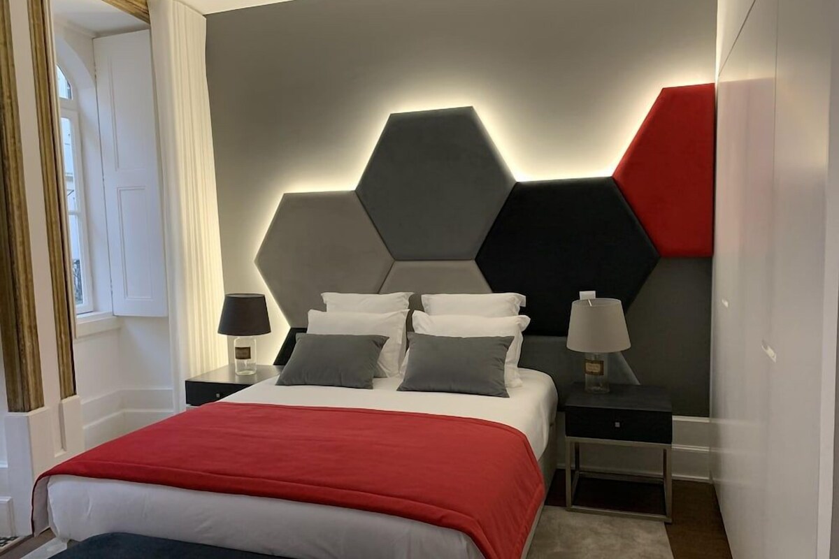 A modern bedroom with a geometric-patterned headboard, a red bedspread, and two bedside tables with lamps.