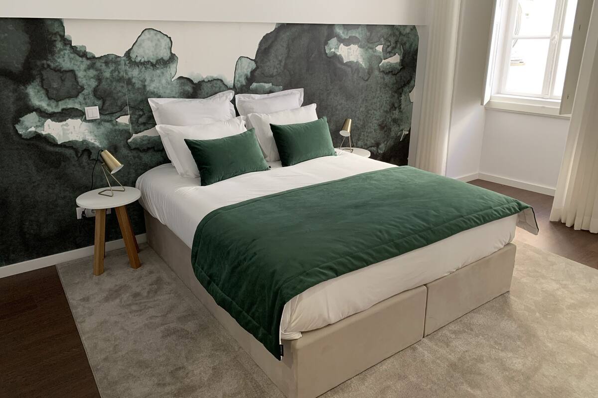 A bedroom with a bed, a nightstand, a lamp, and a large abstract wall mural.