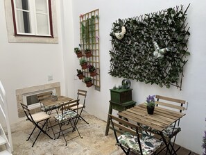 A small patio area with a wooden table and chairs, a potted plant wall, and a decorative wall hanging. - Pharmacia Guest House (Coimbra)